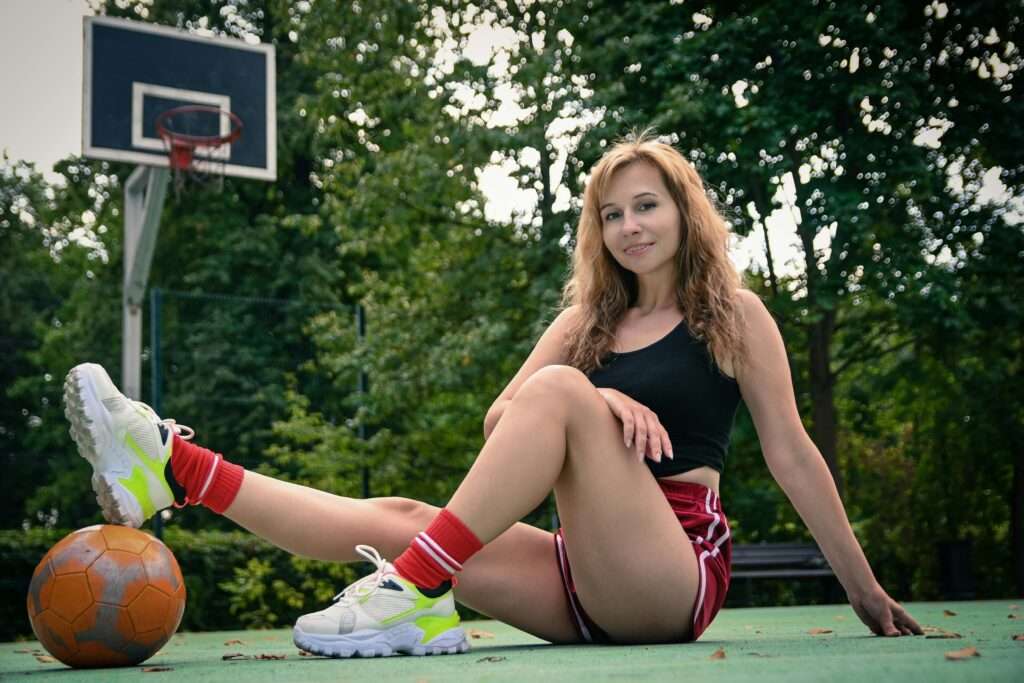 Girl sitting on a basketball on the court, wearing casual athletic attire