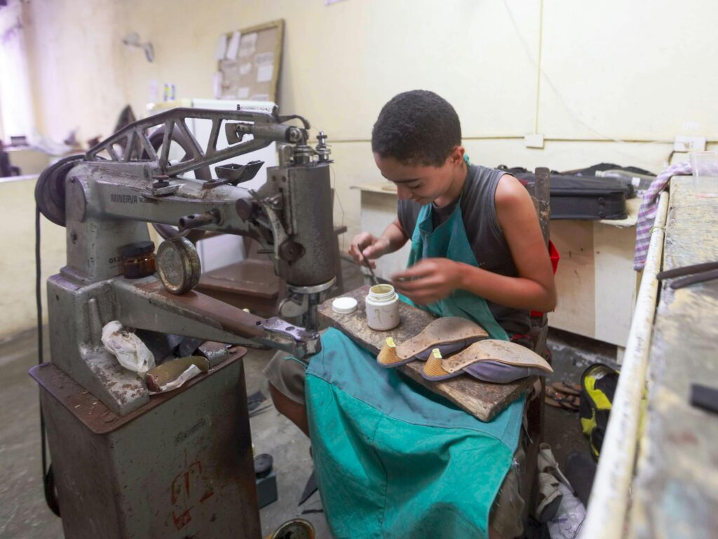 Cobbler repairing a leather handbag alongside shoes on a table